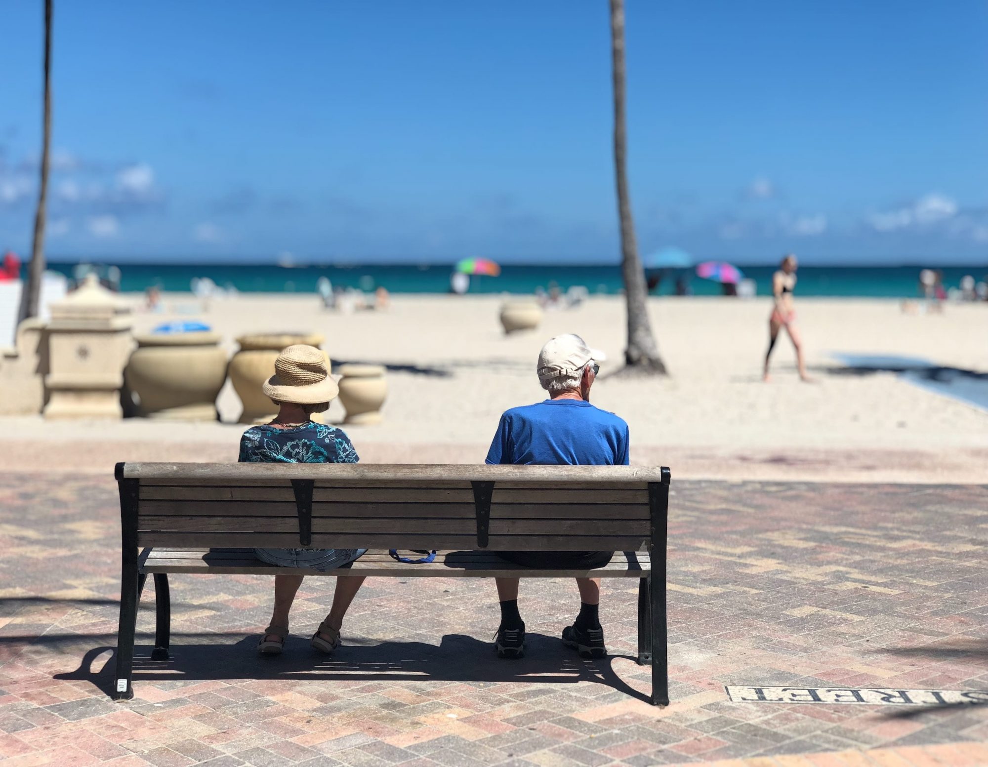Older man and woman sitting on a bench by the beach