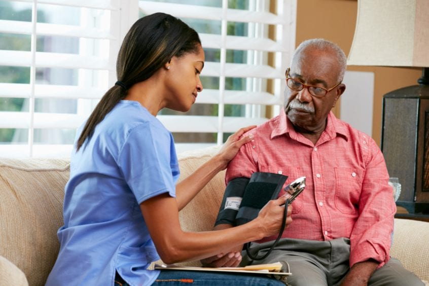 a woman healthcare professional taking the blood pressure of an older man in his home